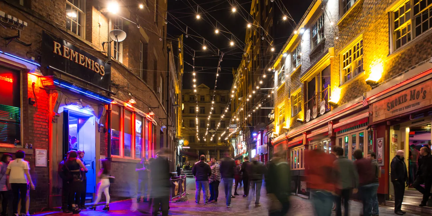 A group of individuals strolling along a dimly lit street during the evening.