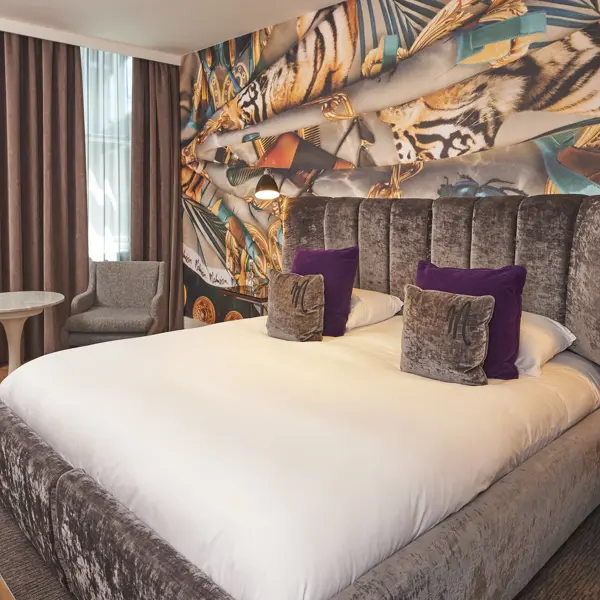 An elegantly furnished hotel room featuring a comfortable bed and stylish chairs.