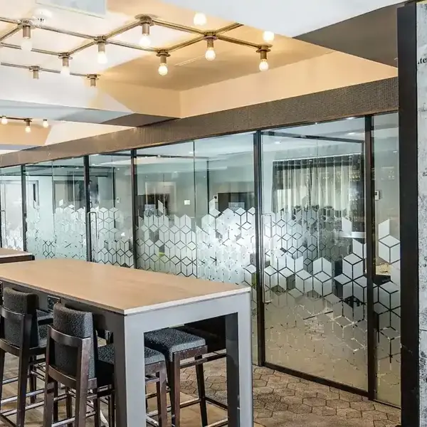 Malmaison Birmingham Work Plus Play Meeting Room  with stencil graffiti adorning a wall, tables with stools, and glass partitioned meeting areas. 