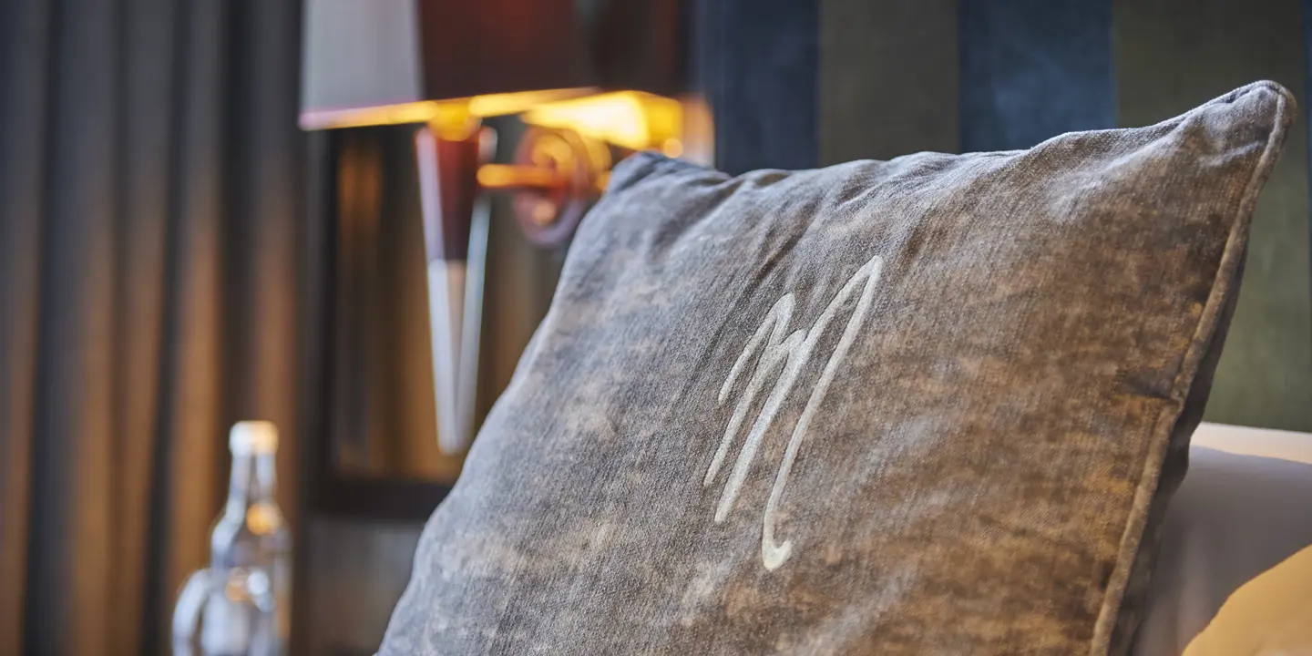 Gray pillow placed on a bed alongside a lamp.