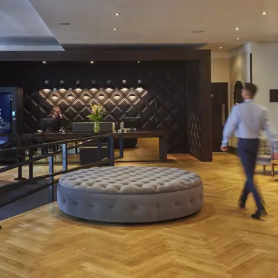 A man strolling through a lobby with a spacious ottoman.