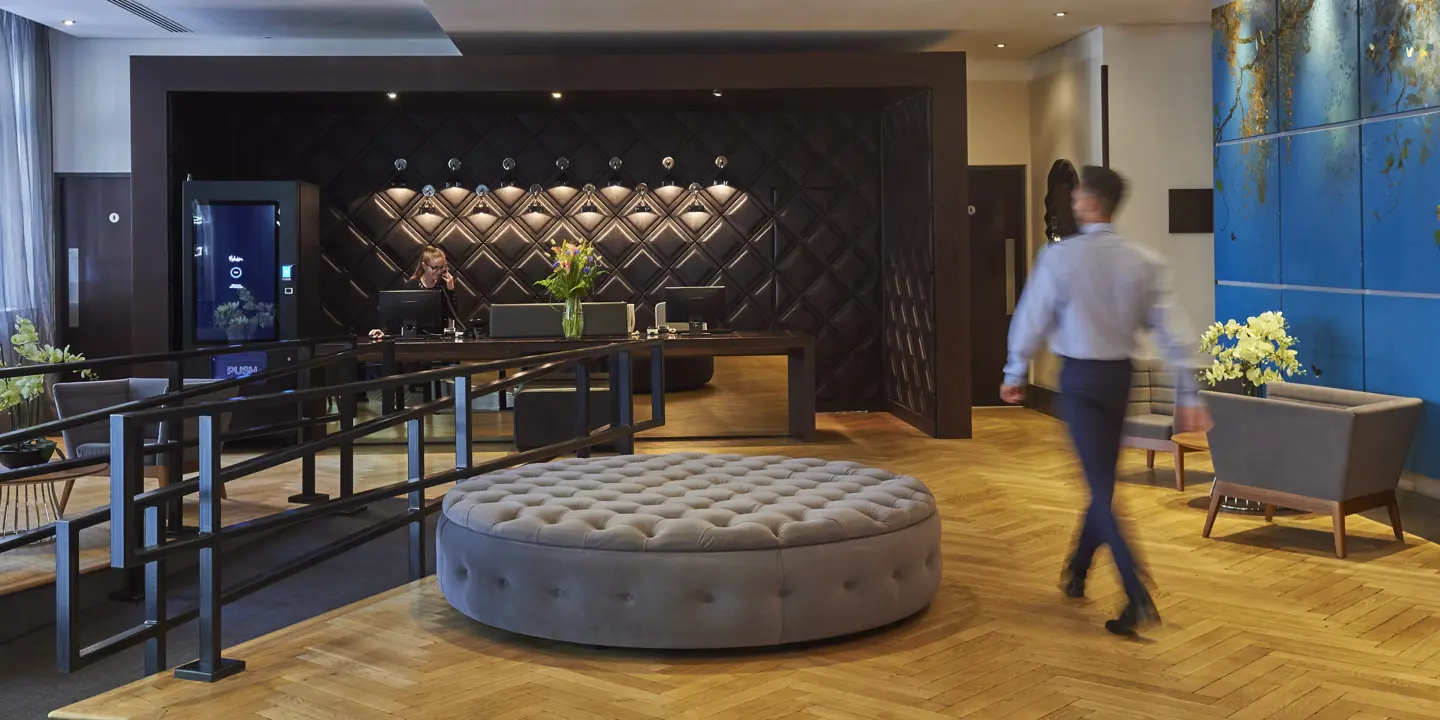 A man strolling through a lobby with a spacious ottoman.