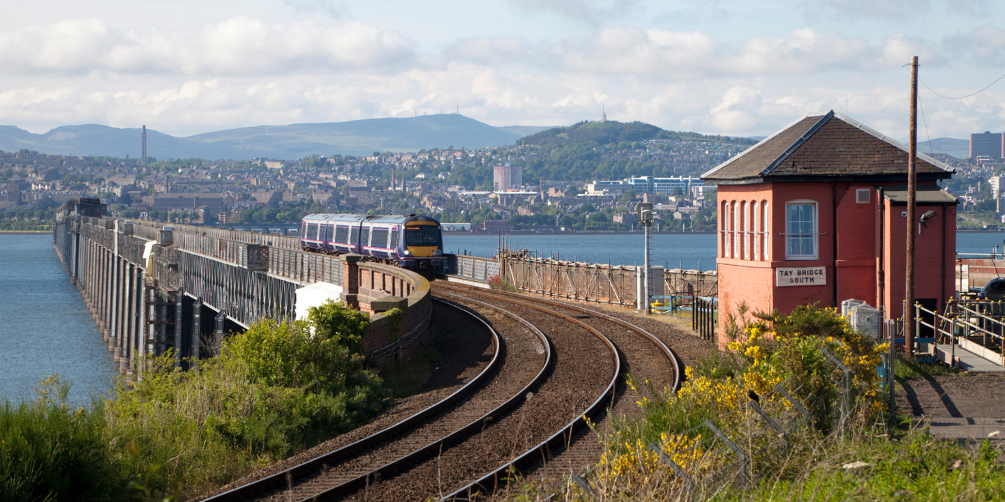 Train traveling along a railway track beside a serene body of water.