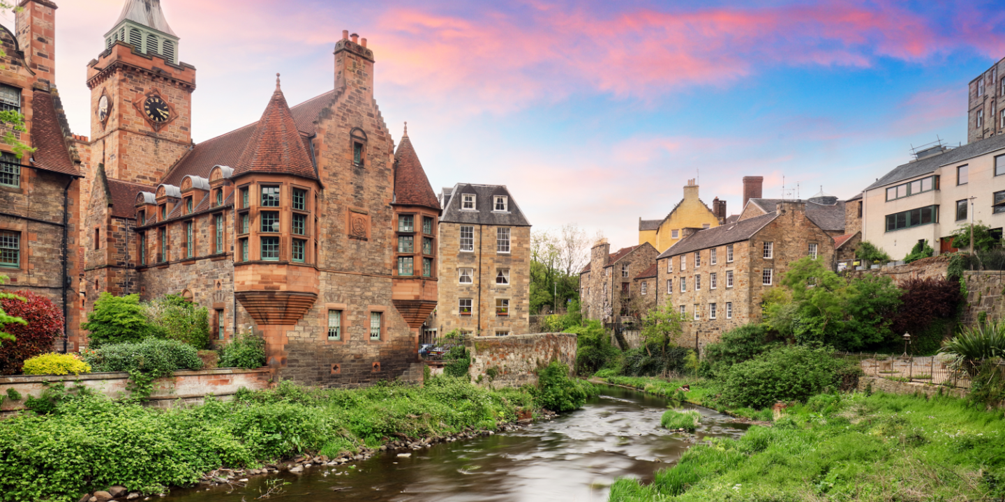 River flowing through a verdant field alongside towering buildings.