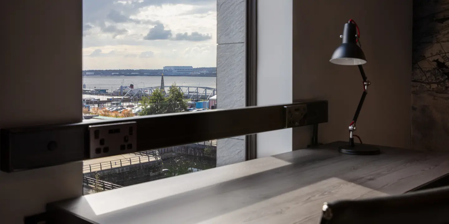 Desk, chair, and lamp positioned in front of a window.