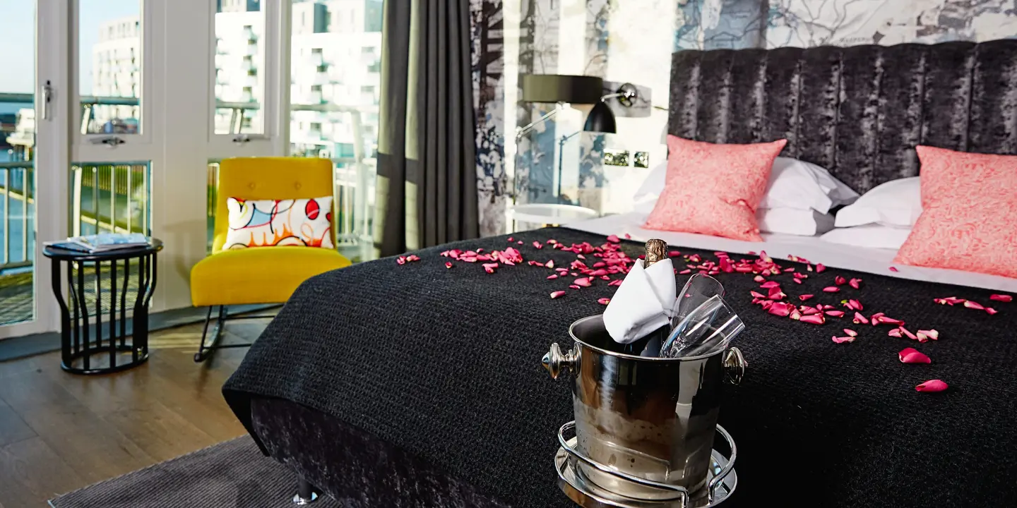 A well-furnished bedroom featuring a comfortable bed decorated with pink petals, a cozy chair, and a large window.