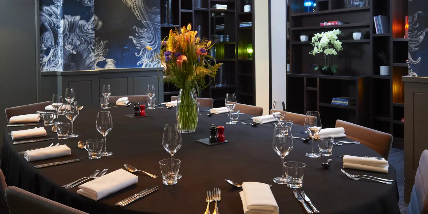 A beautifully arranged dining table with elegantly set place settings and a vase with flowers.