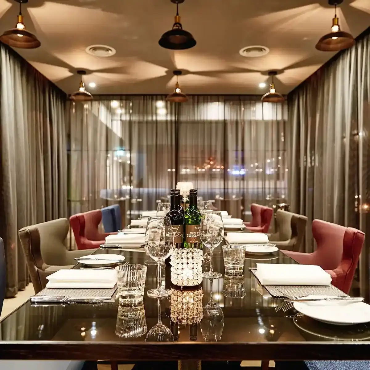 The Cage dining room featuring a spacious table and chairs with wine glasses, bottles of wine, and brass light fixtures.