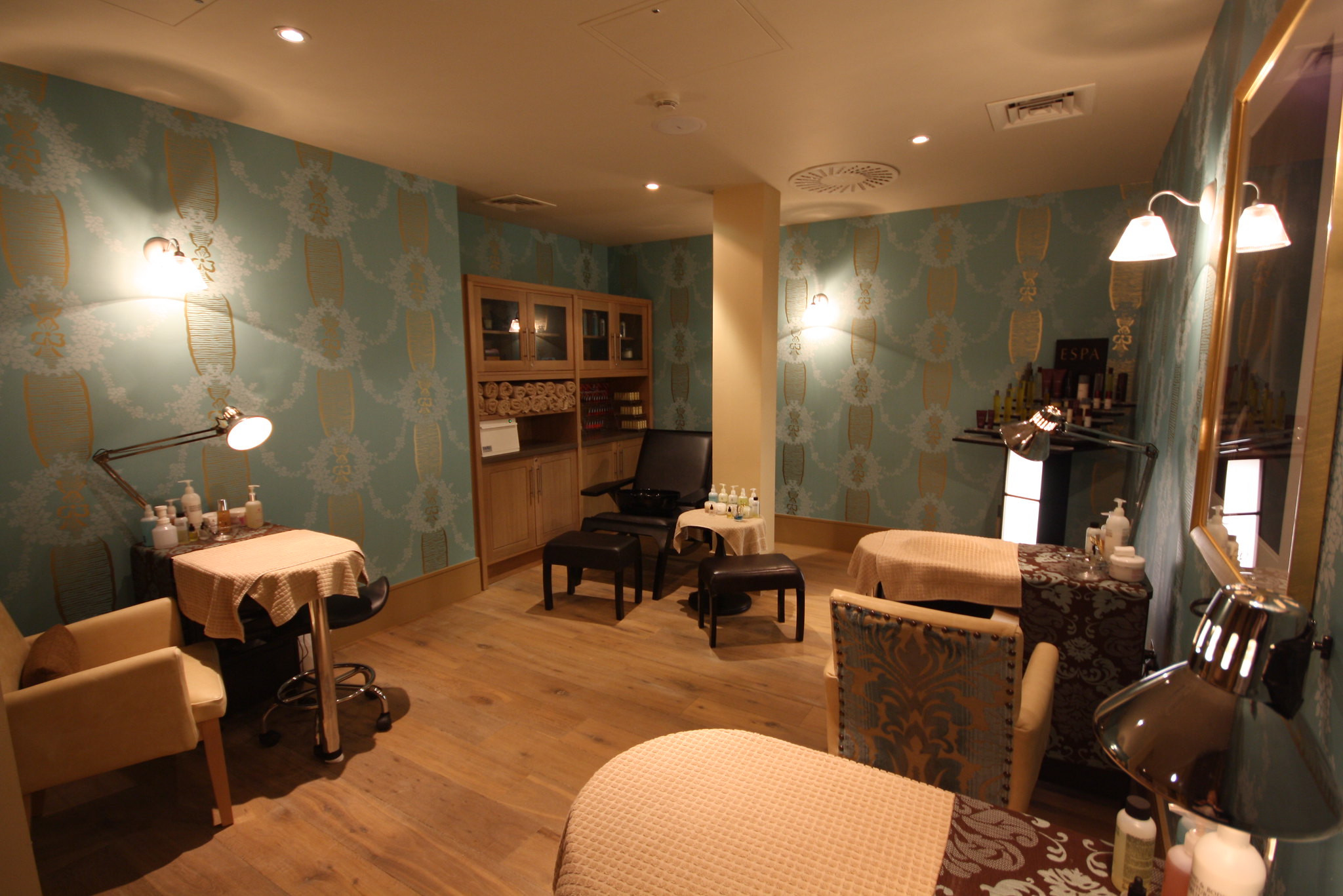 A well-furnished spa treatment room featuring a table, chairs, and a mirror.