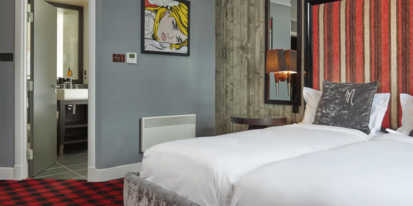 An image of a hotel room featuring two beds and a red carpet.