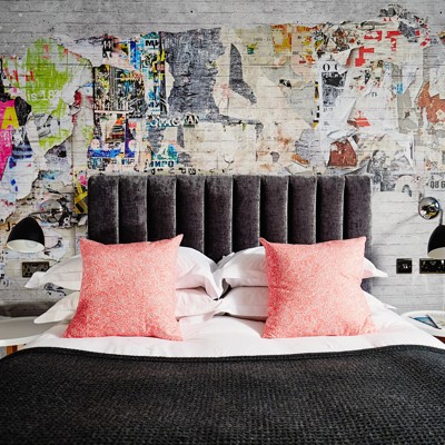 Grey bed with 2 pink pillows and a brightly decorated wall.