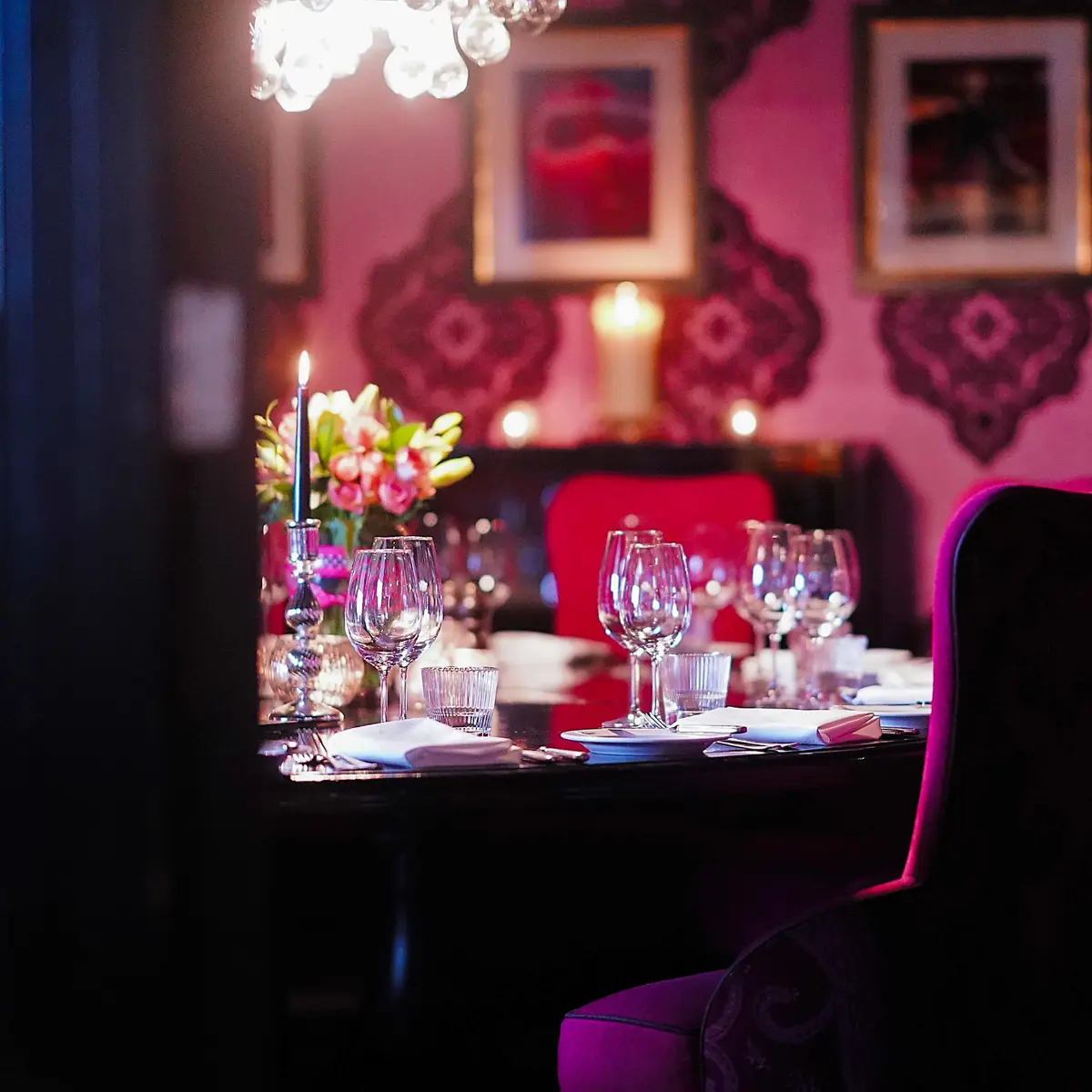 A private dining room with a table featuring several wine glasses, lit candles, flower centrepiece and deep pink seating