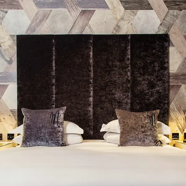 A bed featuring a grey velvet headboard adorned with grey plush pillows.