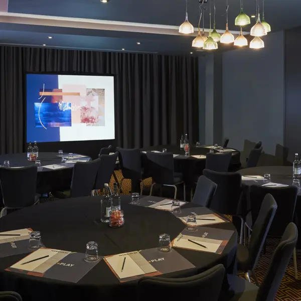 Conference room featuring tables, chairs, and a projector screen.