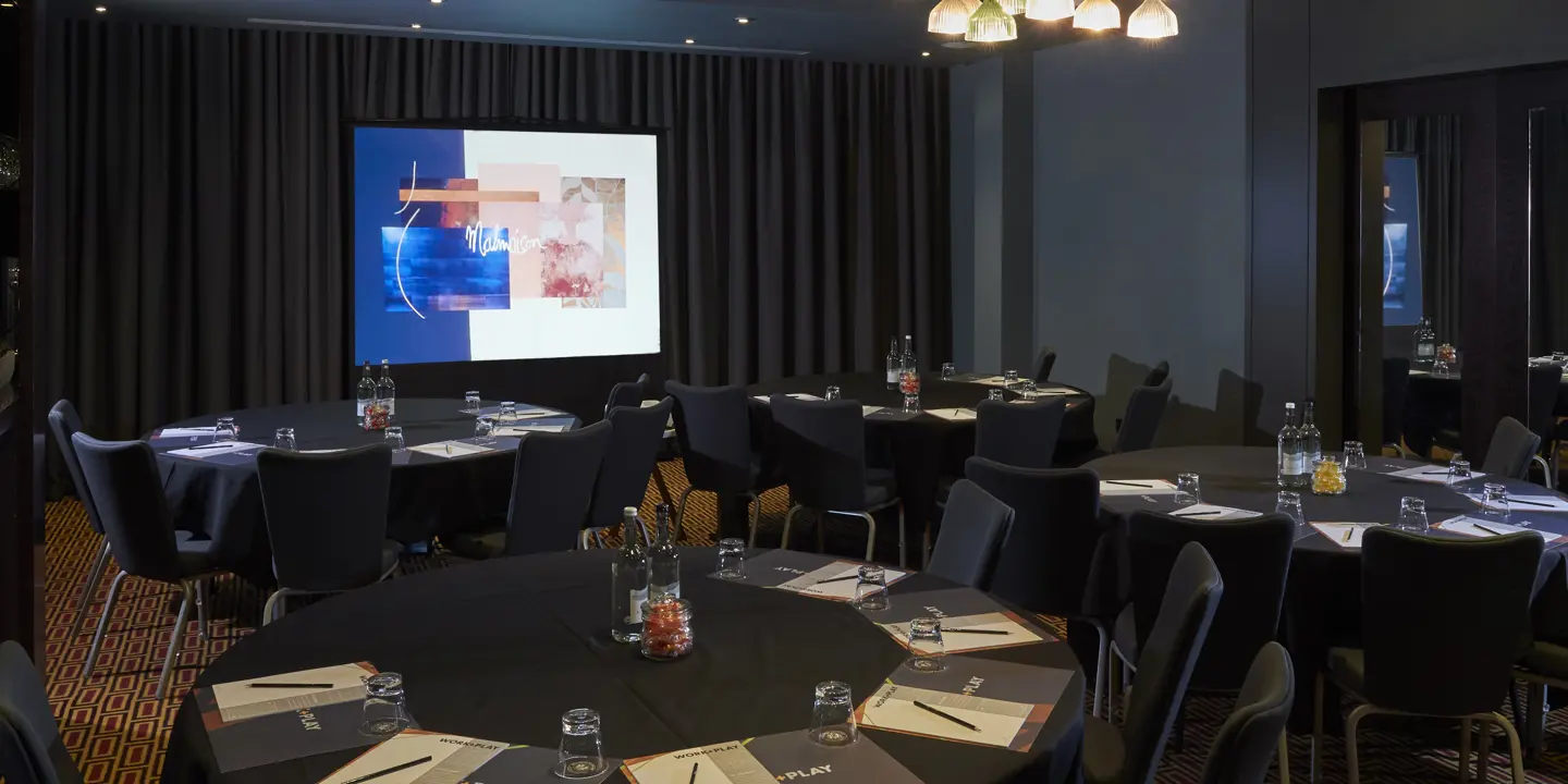 Conference room featuring tables, chairs, and a projector screen.