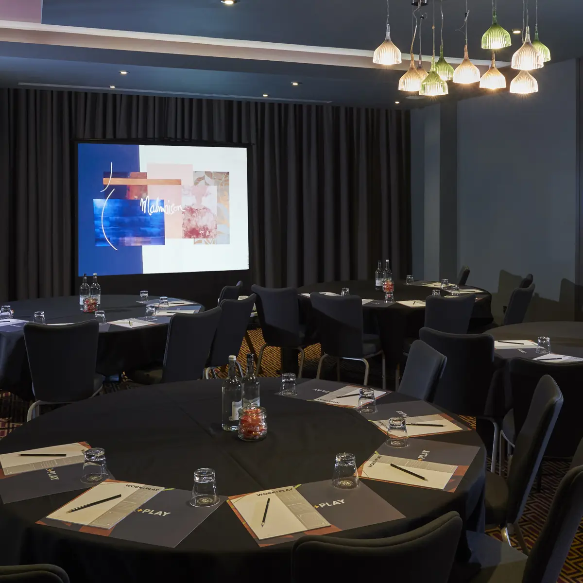 Conference room featuring tables, chairs, and a projector screen.