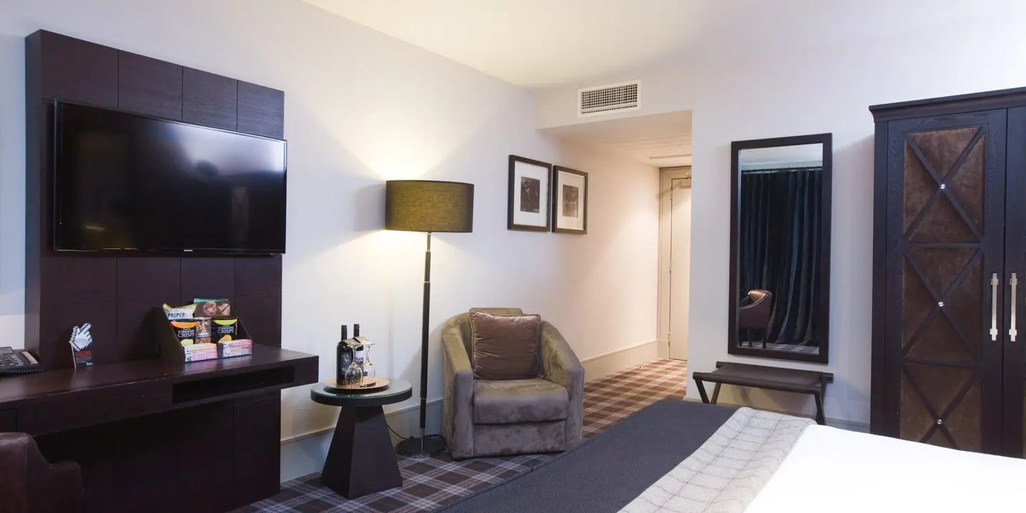 An elegantly furnished hotel room featuring a comfortable bed, spacious desk, and modern television.