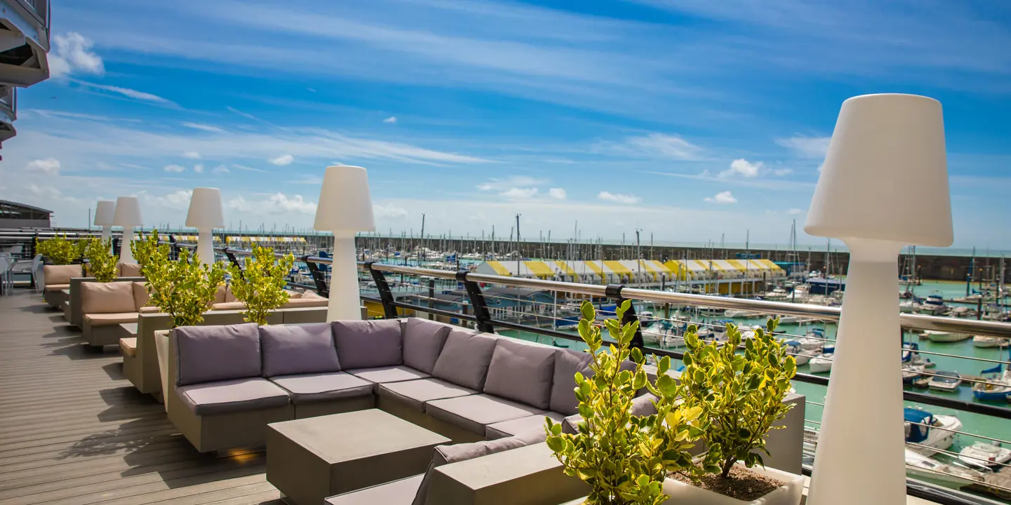 A wooden deck balcony overlooking Brighton Marina, complete with cushioned seating, and feature lighting.