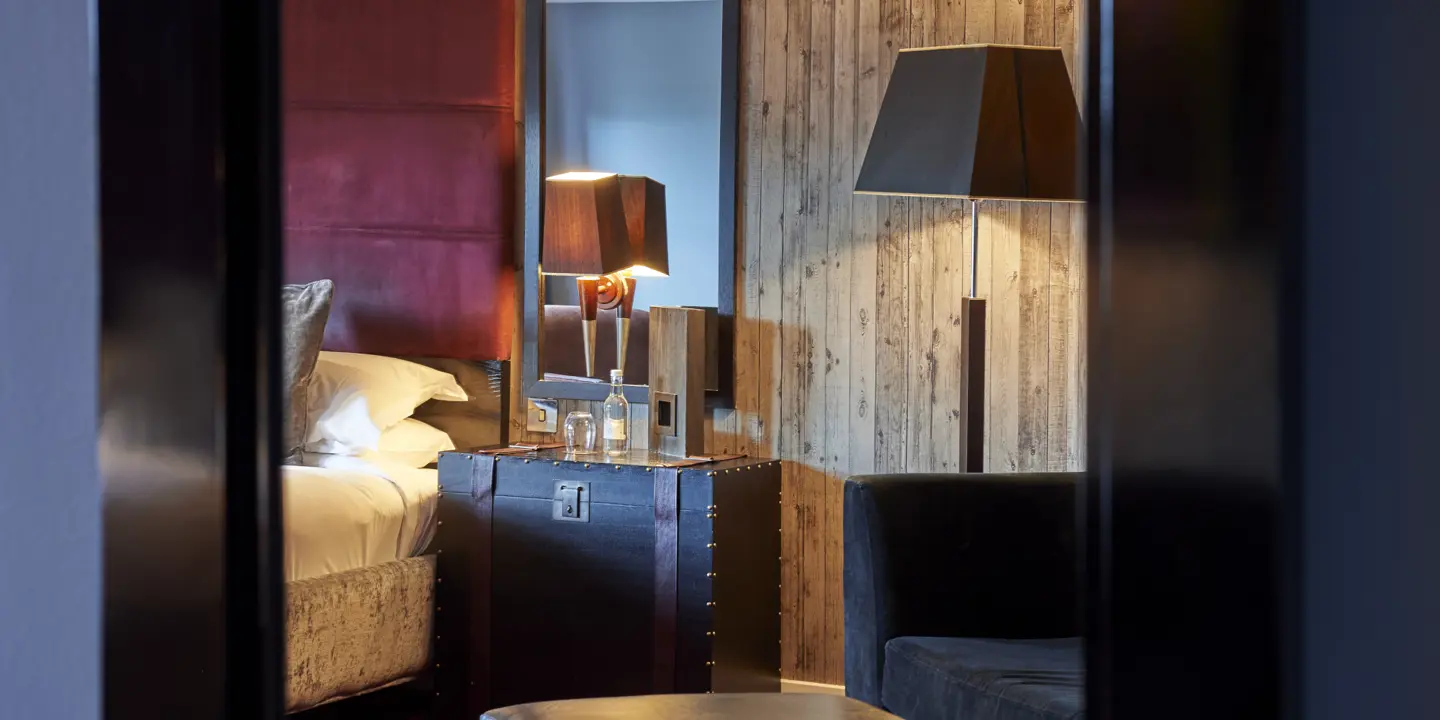 An elegant nightstand and lamp positioned next to a red velvet bed.