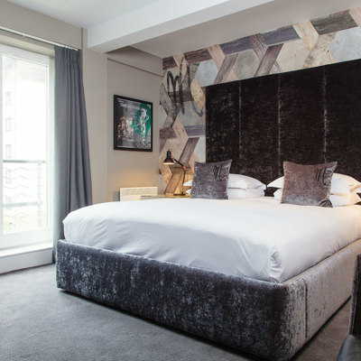 A grey velvet bed positioned in a bedroom adjacent to a window.