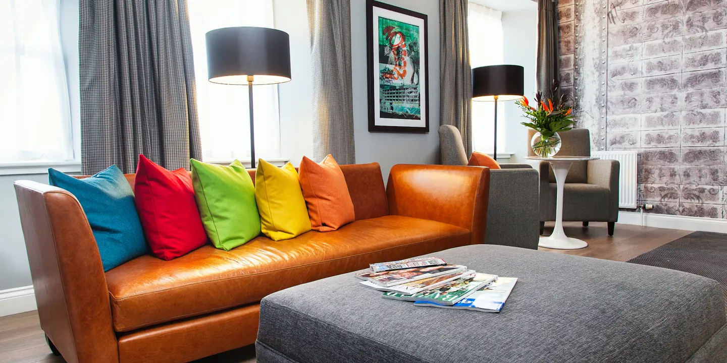 A brown leather sofa lined with multi-coloured cushions.