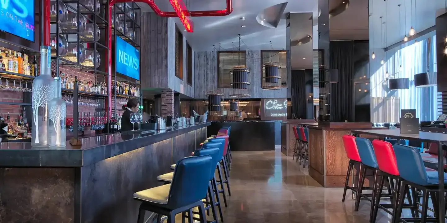 Birmingham Malmaison bar with grey granite bar top, leather stools lining the bar and several tables with seating are visible.