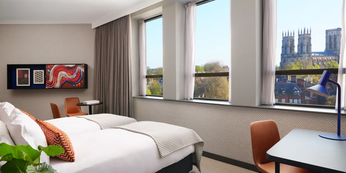 Bedroom featuring a large bed, desk with orange leather chair and large windows.