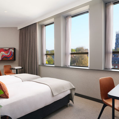 Bedroom featuring a large bed, desk with orange leather chair and large windows.