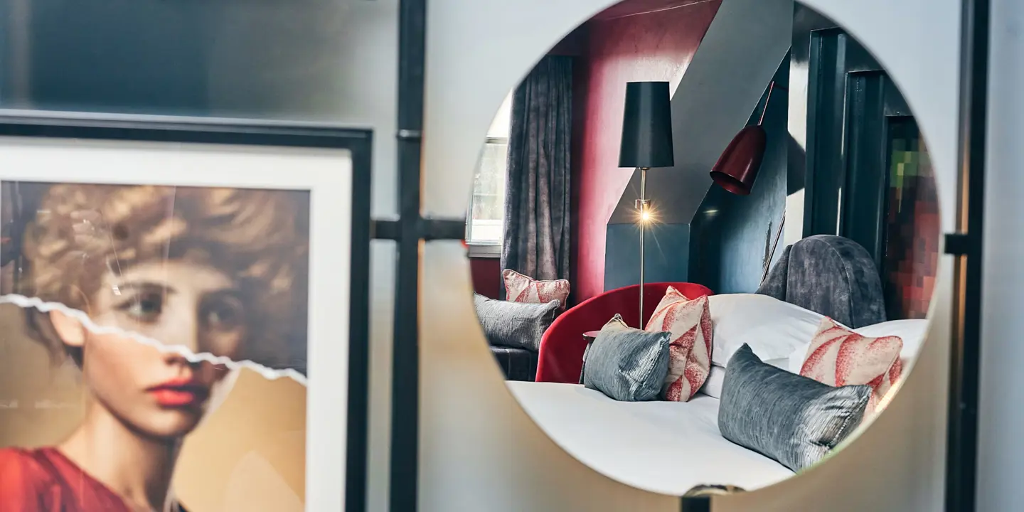 Reflection of a bedroom in a mirror alongside a painting.