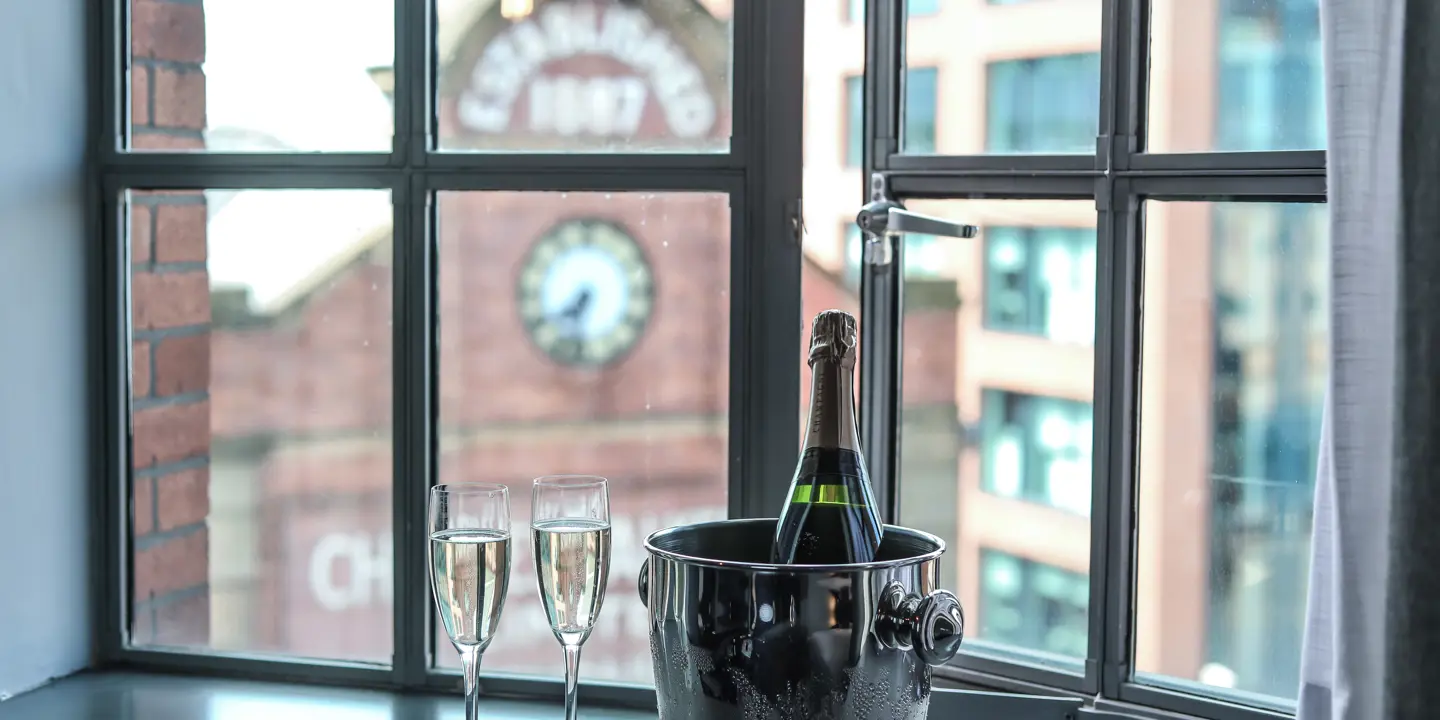 A bottle of champagne and two glasses resting on a windowsill.