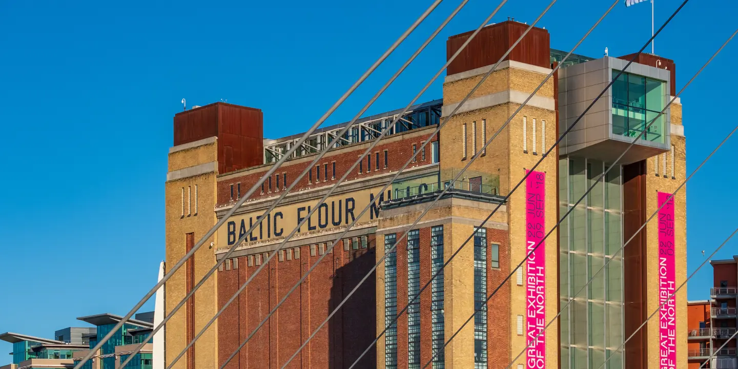 Individuals strolling across a bridge with a building in the backdrop.