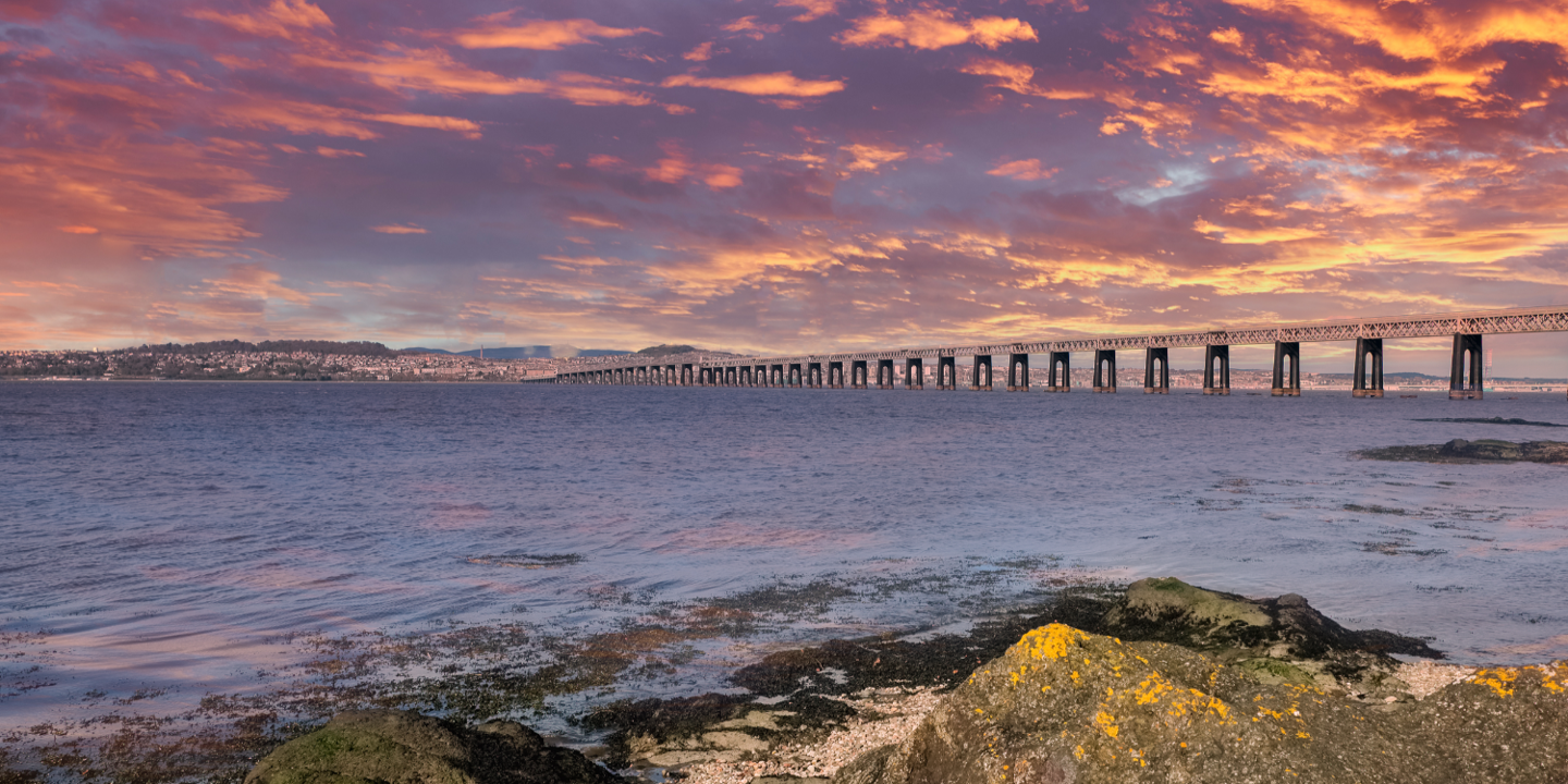 Scenic view of a serene ocean sunset with a bridge in the background.