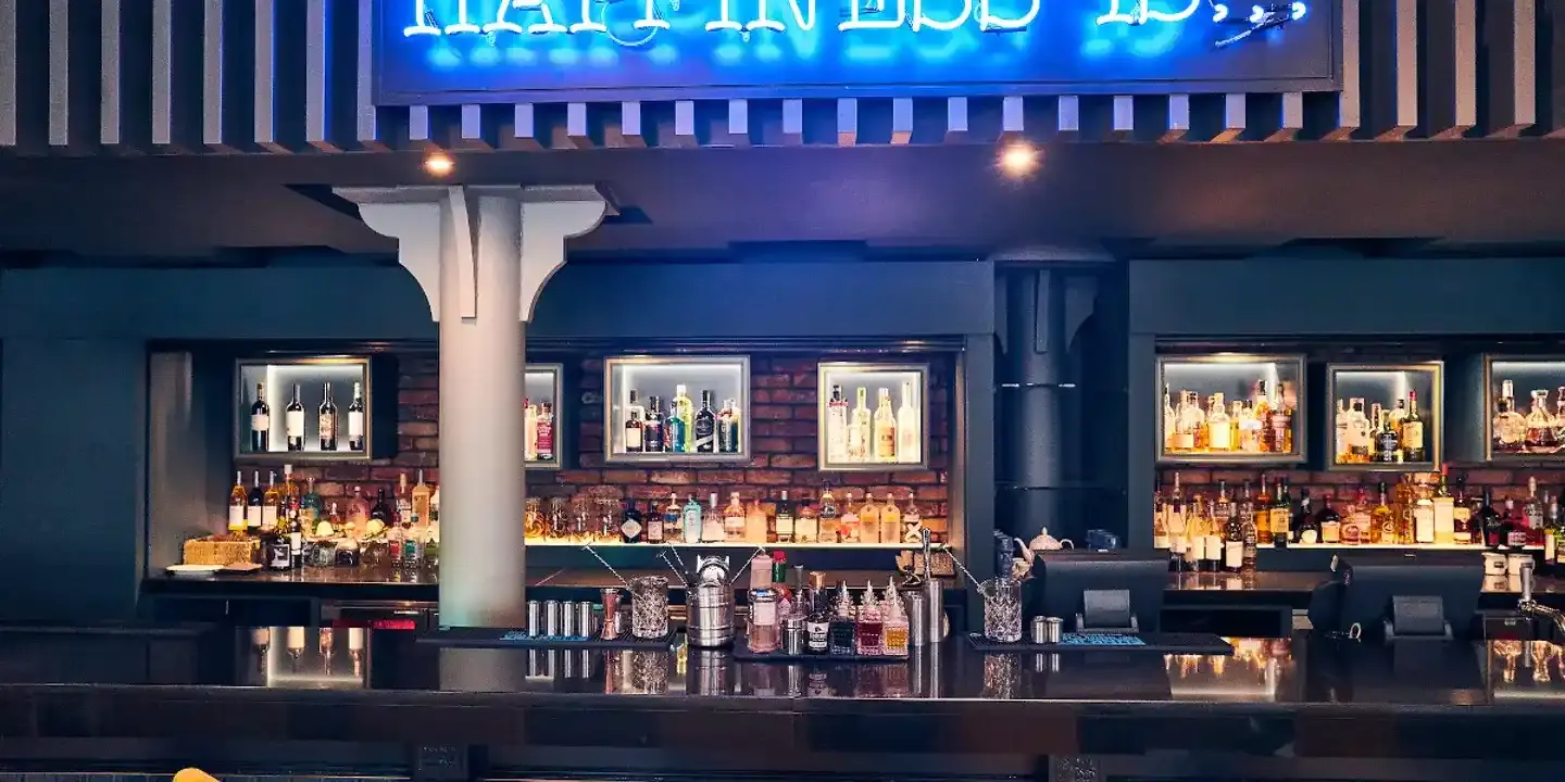 Belfast bar with bottles of alcohol neatly displayed on shelves lining an exposed brick wall. A blue neon sign is seen partially overhead.