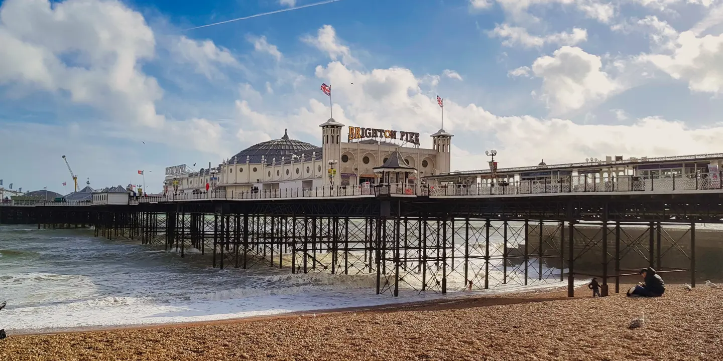 A view of Brighton beach and pier with individuals seated on the beach and waves lapping the shore.