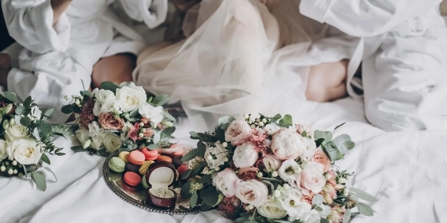 Bridesmaids sitting together on a bed with bouquets of flowers in front of them.