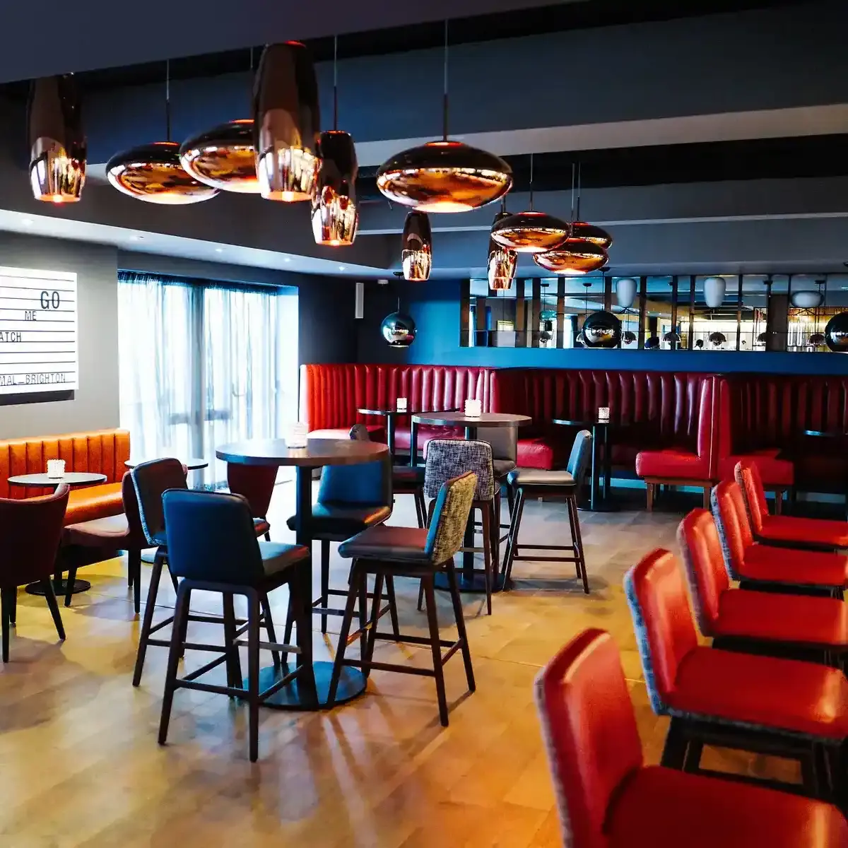 A bar featuring numerous tables and chairs, booth seating areas, and feature copper light fittings.