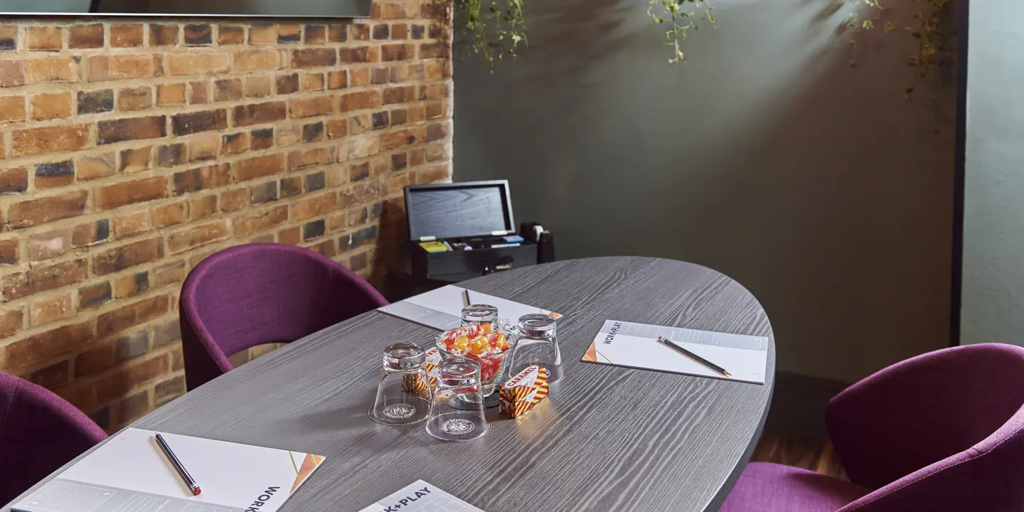 Table with purple chairs against a brick wall.