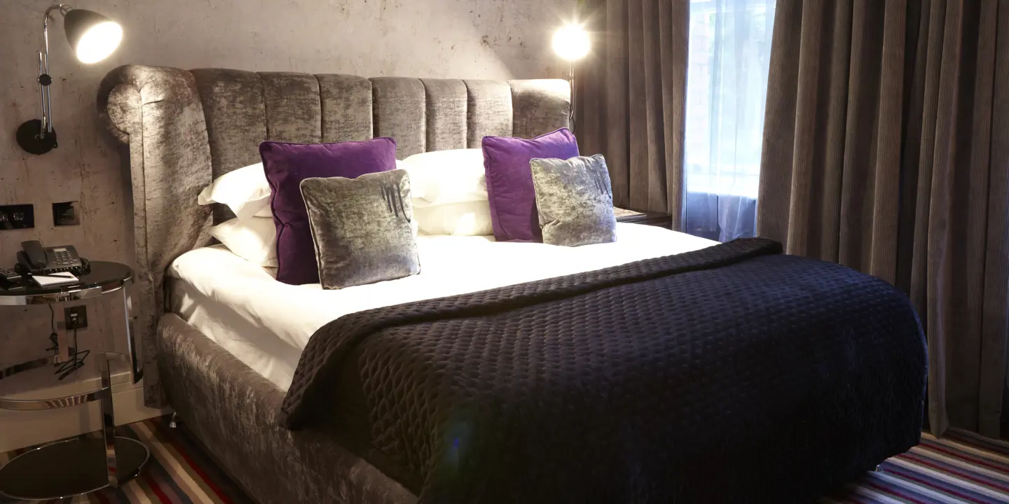 Bedroom featuring a comfortable bed and a nightstand with an accompanying lamp.