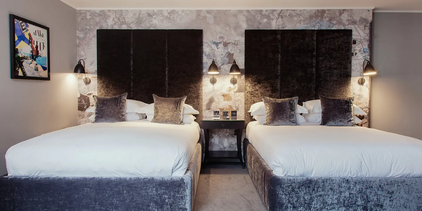 Two beds placed side by side with grey velvet headboards.