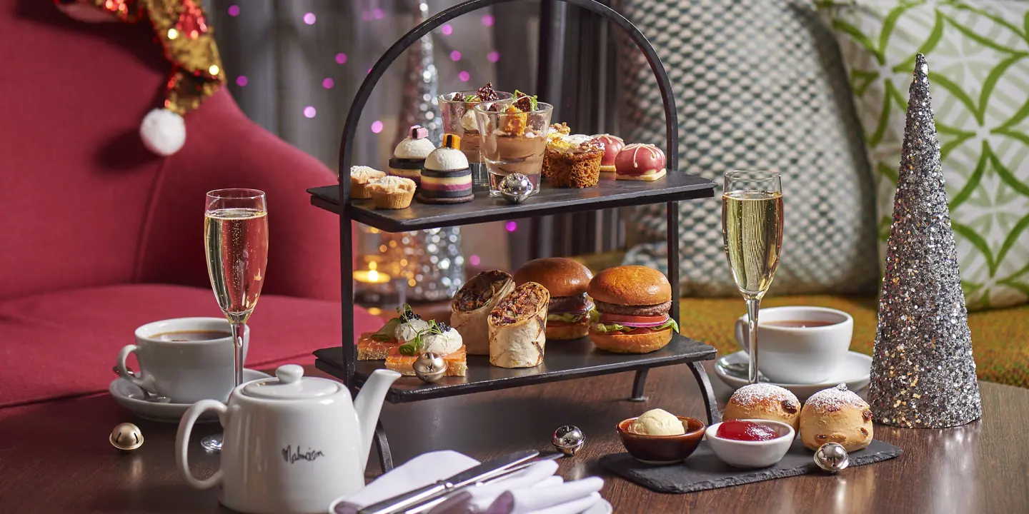 A table displaying a tray of appetizing food accompanied by a glass of fine wine and Christmas decorations in the background.