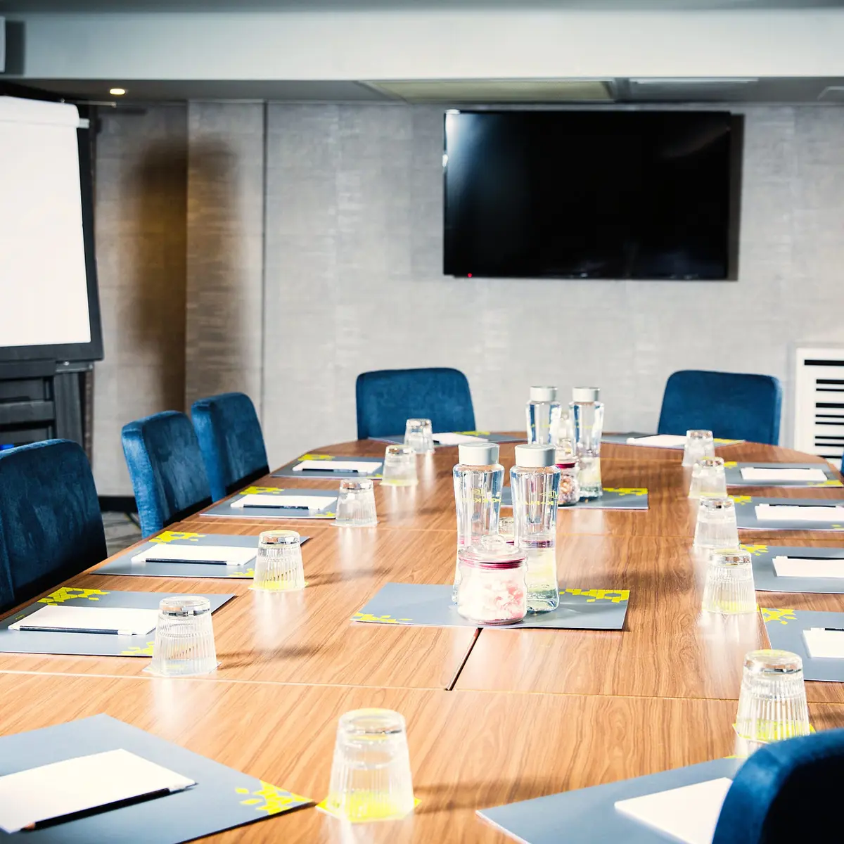 Conference table featuring blue chairs and a flat screen TV.