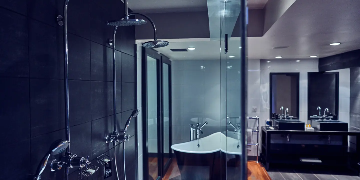 Black bathroom with shower, free standing bath and dual sinks.